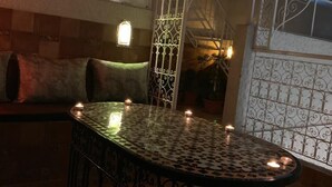 A cozy lounge area with a round table surrounded by candles, a patterned wall, and a window with a view. - Riad Najiba (Rabat)