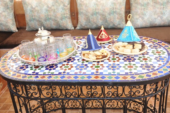 Et rundt bord med mosaikbordplade, en bakke med glas og snacks, samt to dekorative kegleformede hatte.