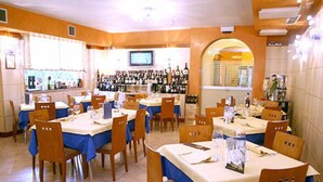 Ein Restaurant mit mehreren Tischen und Stühlen, einer Bar mit zahlreichen Flaschen sowie einem Fernseher an der Wand.