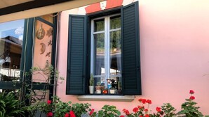 Ein Gebäude mit einer rosafarbenen Fassade, einem Fenster mit grünen Fensterläden und roten Blumen davor.