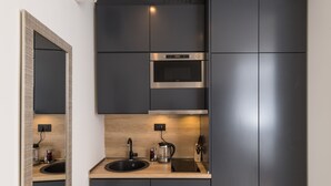 Une cuisine moderne avec des meubles de rangement sombres, un four encastré, un four à micro-ondes et un évier avec une bouilloire.