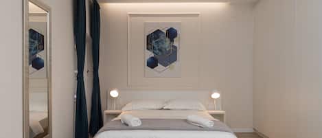 A modern bedroom with a wooden bed, white bedding, a large mirror, and abstract wall art.