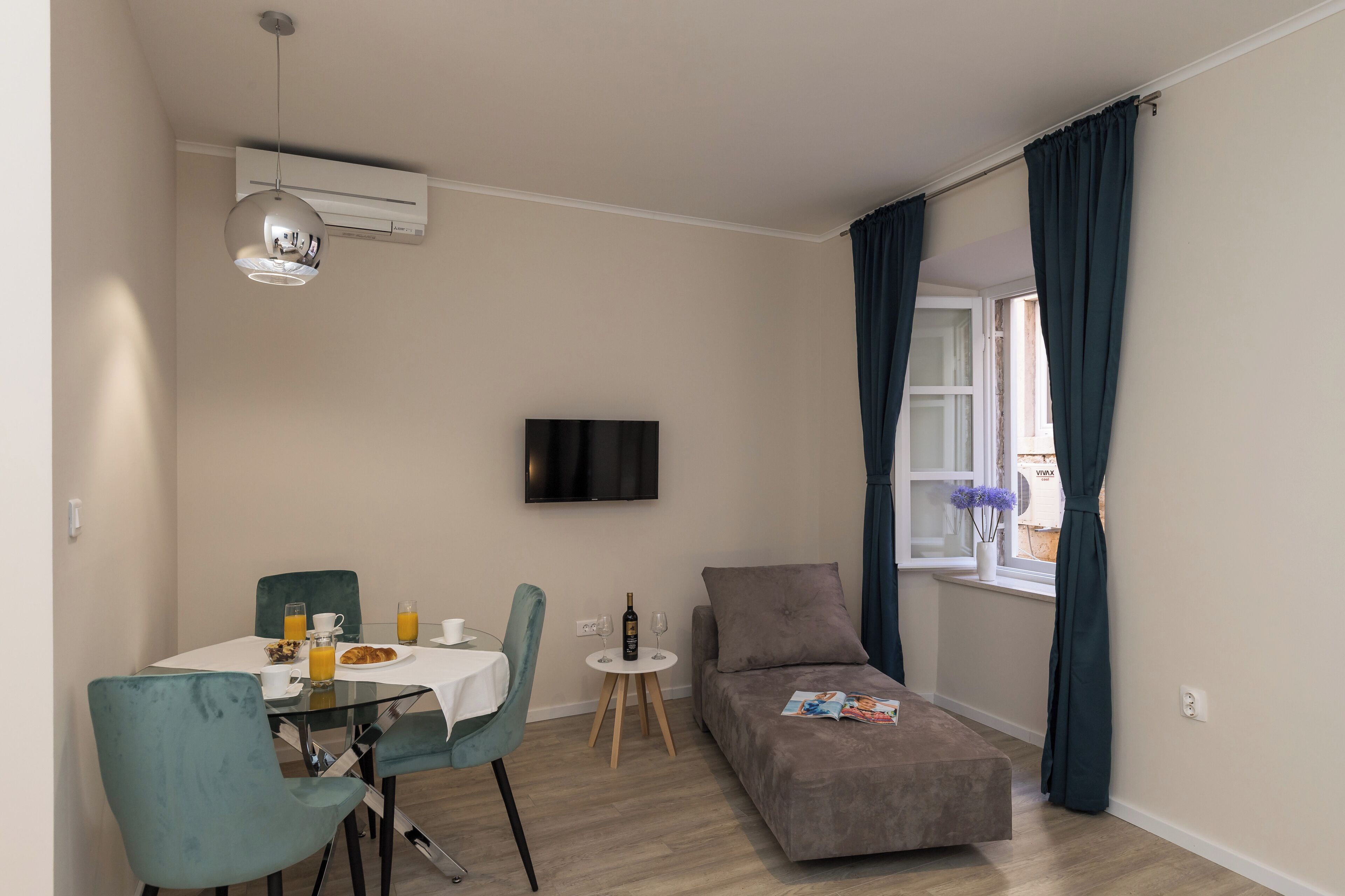 A compact living space with a dining area, a sofa, a TV, and a window with curtains.
