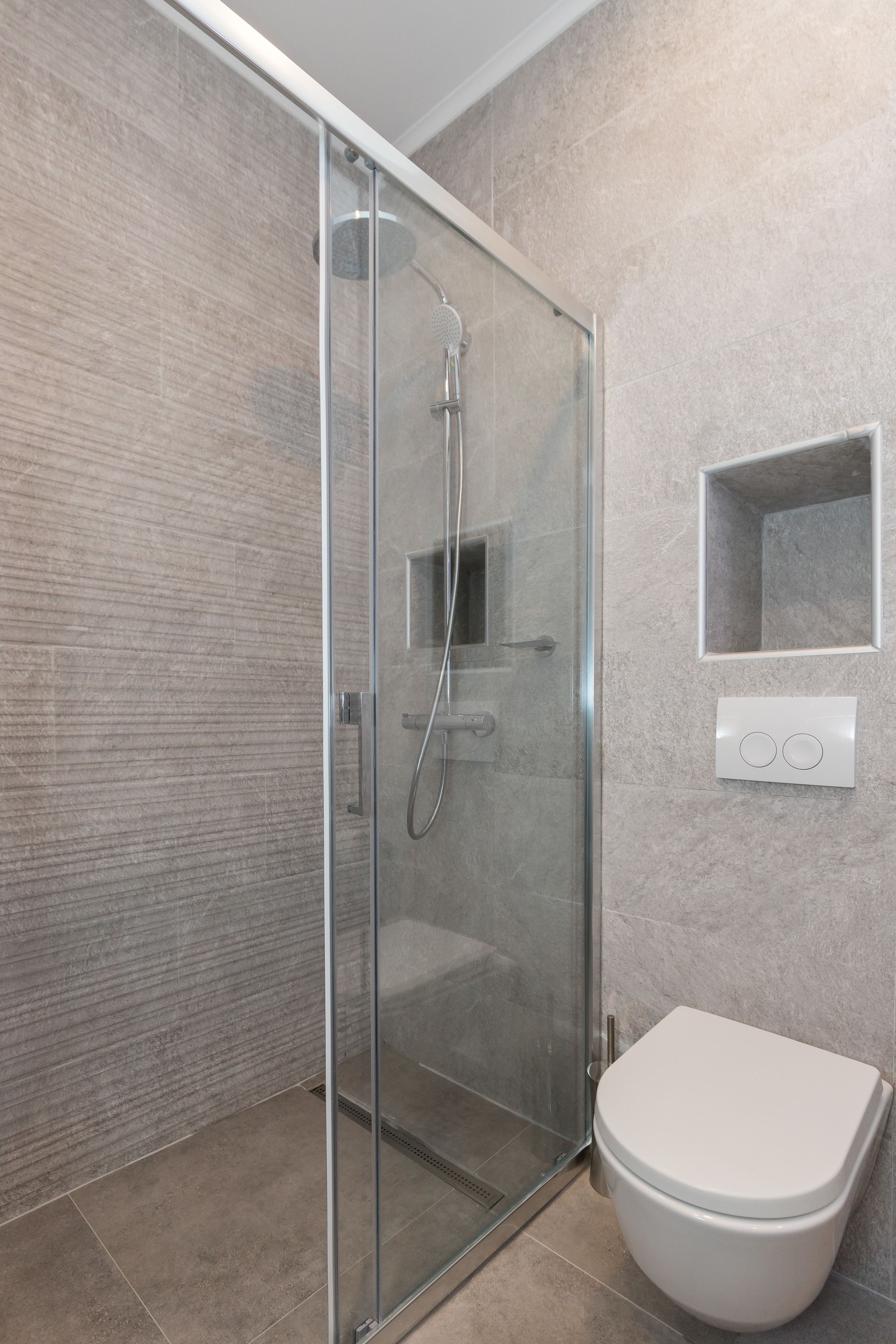 A modern bathroom with a glass-enclosed shower, a white toilet, and a small mirror.