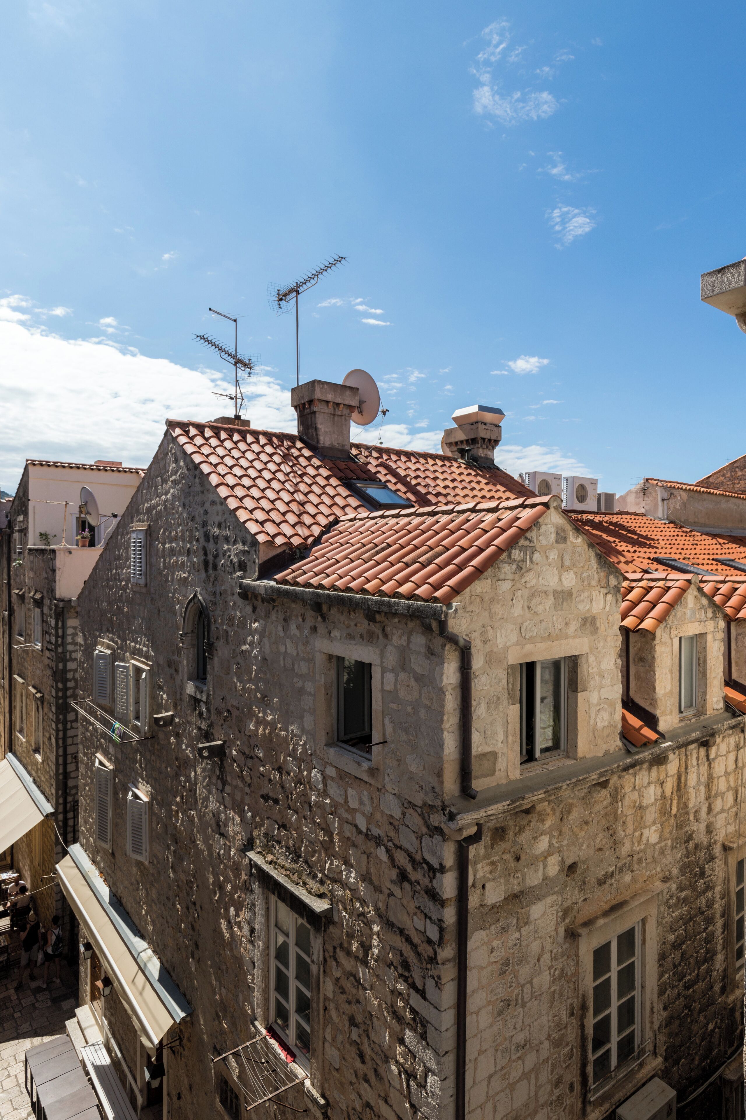 A stone building with a tiled roof, multiple chimneys, and satellite dishes.