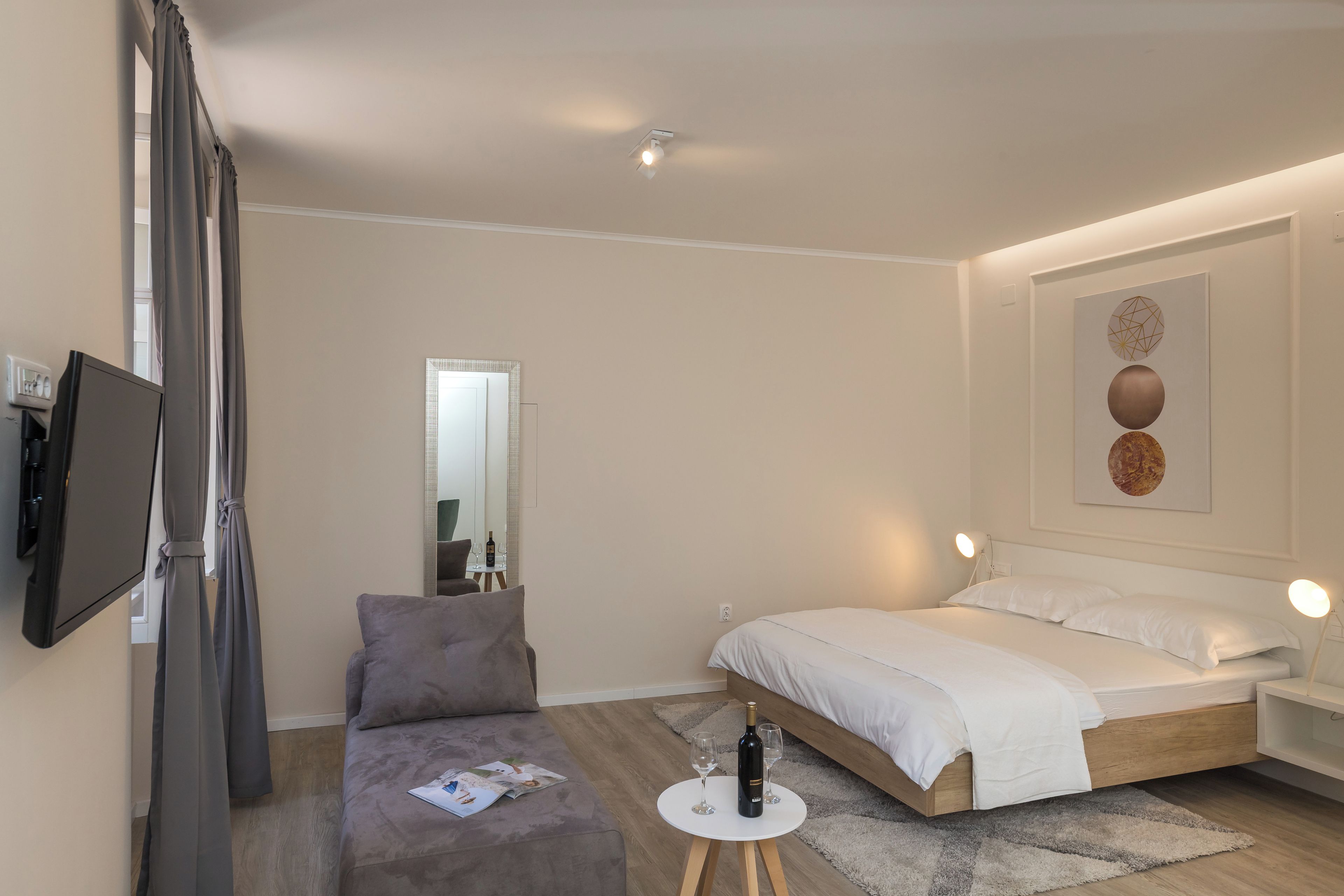 Ein modernes Schlafzimmer mit einem Bett, einem kleinen Tisch mit Flasche und Gläsern, einem Fernseher und einem Sofa.