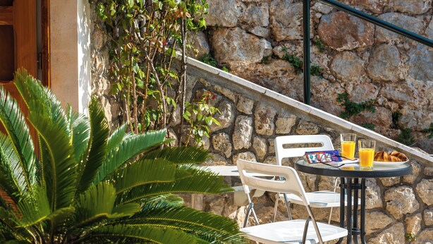 An outdoor seating area with a stone wall, white chairs, a table, and a glass of orange juice. - Romance Apartment Dubrovnik (Dubrovnik)