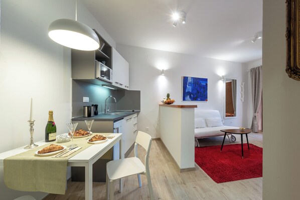 Una cocina moderna con armarios blancos, una mesa de comedor con alfombra roja y un sofá blanco en la sala de estar.