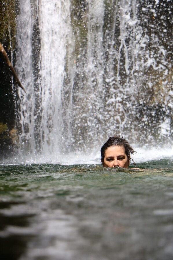 Una persona nada en un cuerpo de agua, con una cascada al fondo.