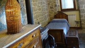 A rustic bedroom with a stone wall, a wooden dresser, a bed with a headboard, a window with a view, and a radiator. - Agriturismo Arcera (Roccafluvione)