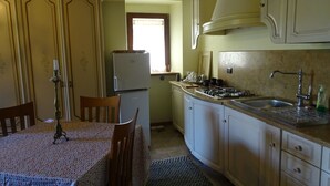 A compact kitchen with a dining table, chairs, a refrigerator, a stove, and a sink. - Agriturismo Arcera (Roccafluvione)