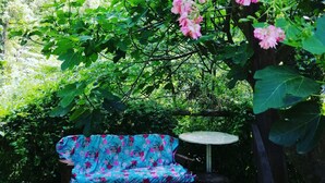 A garden with a wooden bench and a table, surrounded by lush greenery and pink flowers. - Agriturismo Arcera (Roccafluvione)