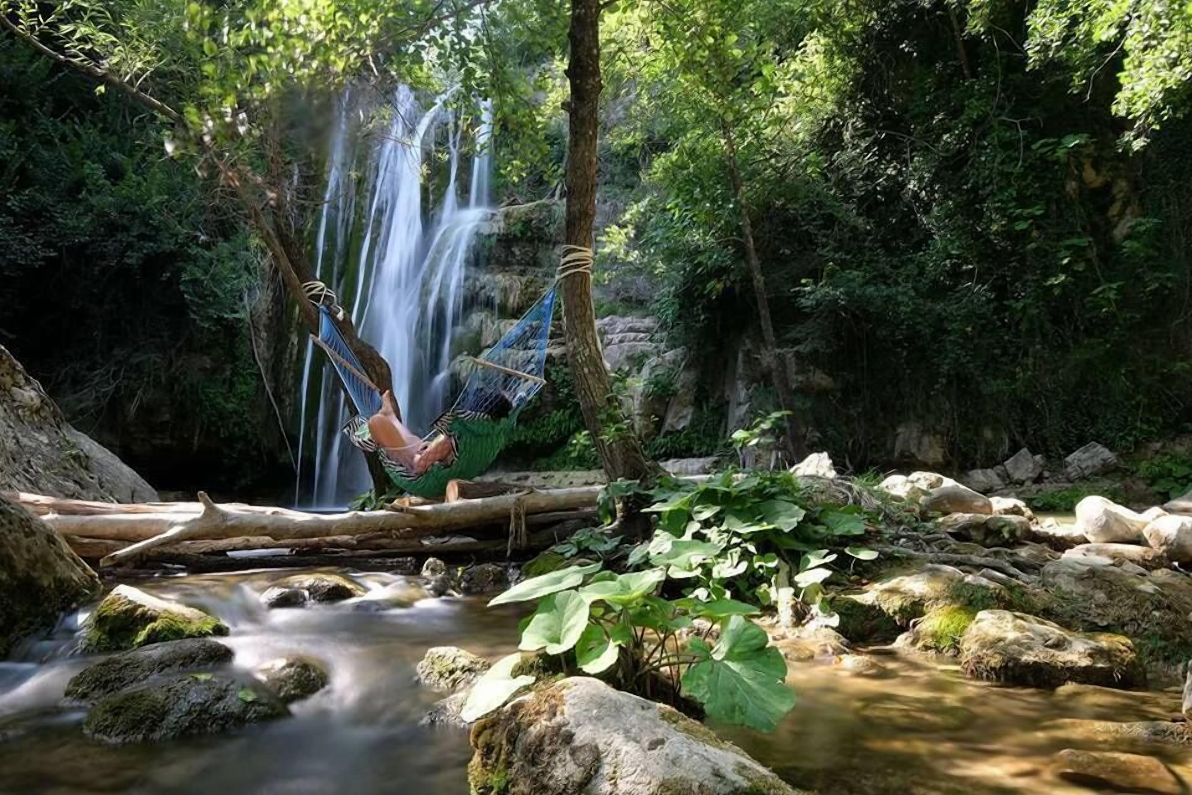 Una hamaca suspendida sobre una cascada en una zona boscosa, con un arroyo debajo.