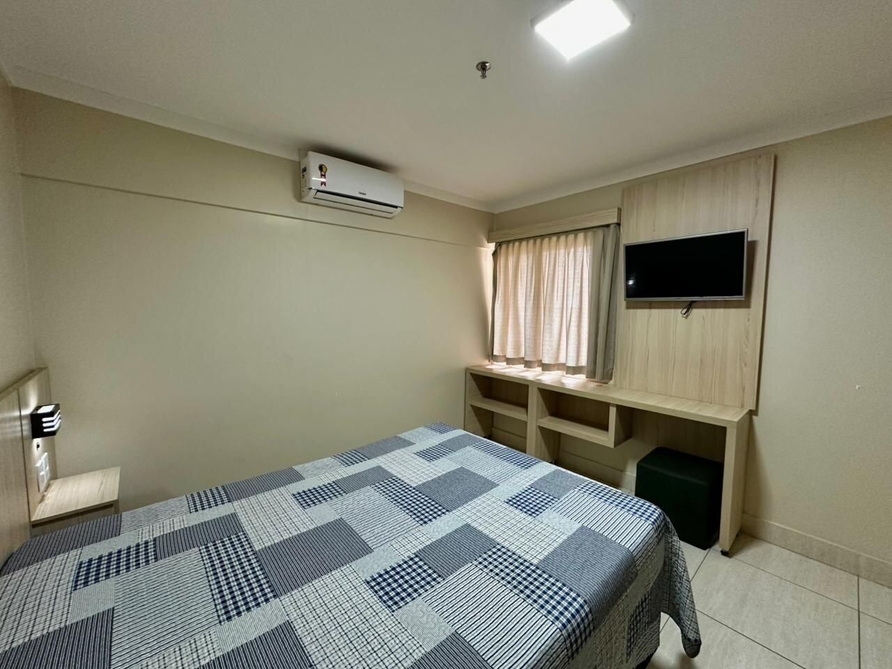 Een hotelkamer met een bed, een bureau met stoel, een televisie en een airconditioning.