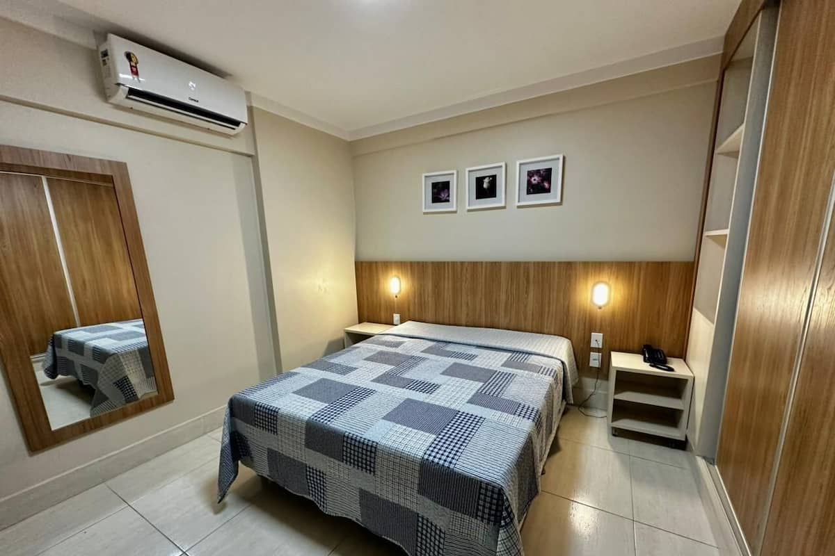 A bedroom with a bed, bedside tables, a mirror, and an air conditioning unit.