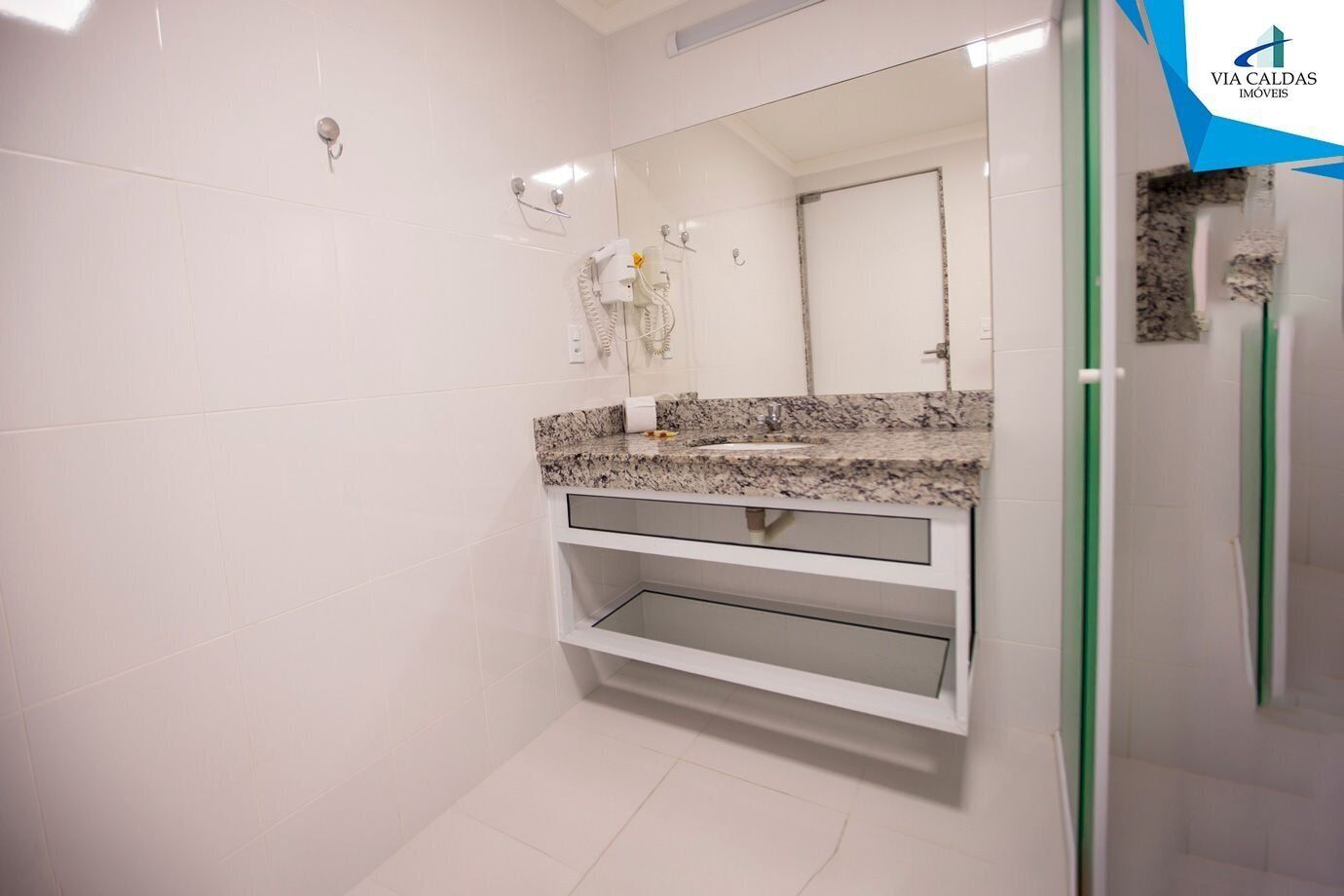 Un baño con azulejos blancos, encimera de granito, un espejo y zona de ducha.