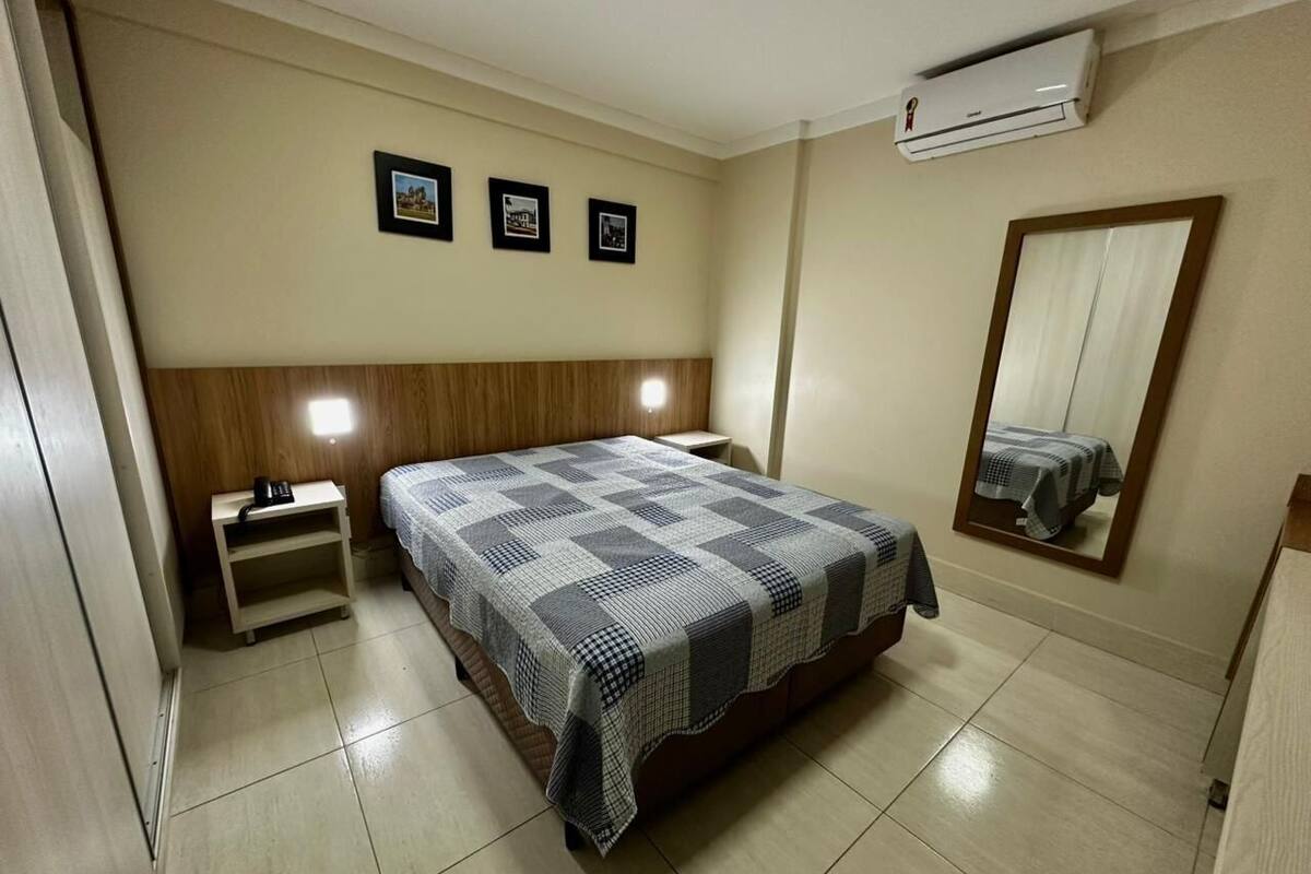 A bedroom with a bed, bedside tables, a wardrobe, a mirror, and an air conditioning unit.