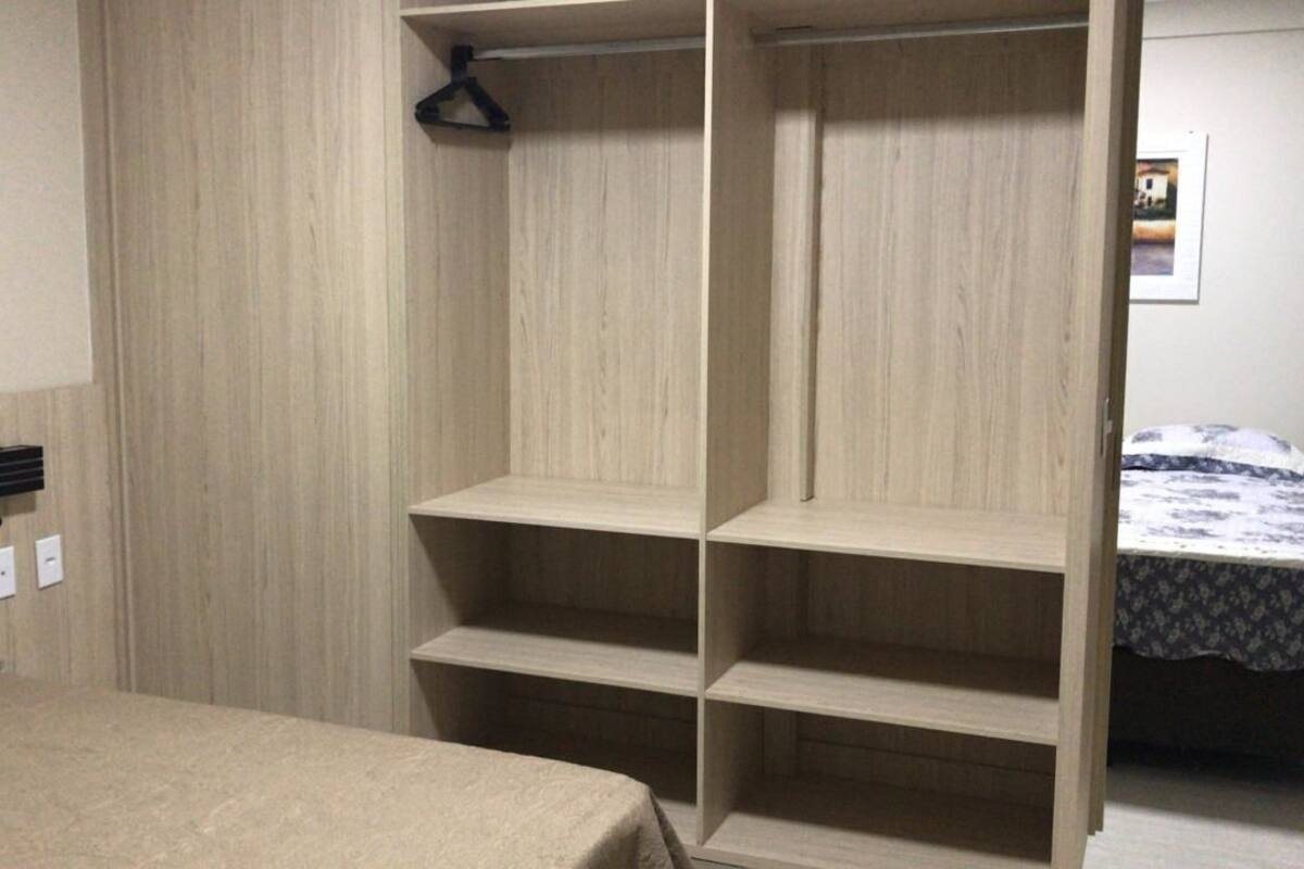 A bedroom with a bed, a wooden wardrobe with multiple shelves, and a small bedside table.
