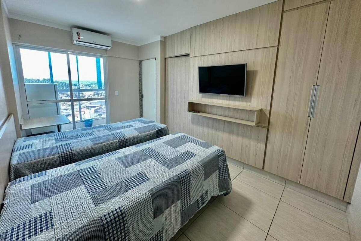 A room with two beds, a TV mounted on the wall, and a window with a view.