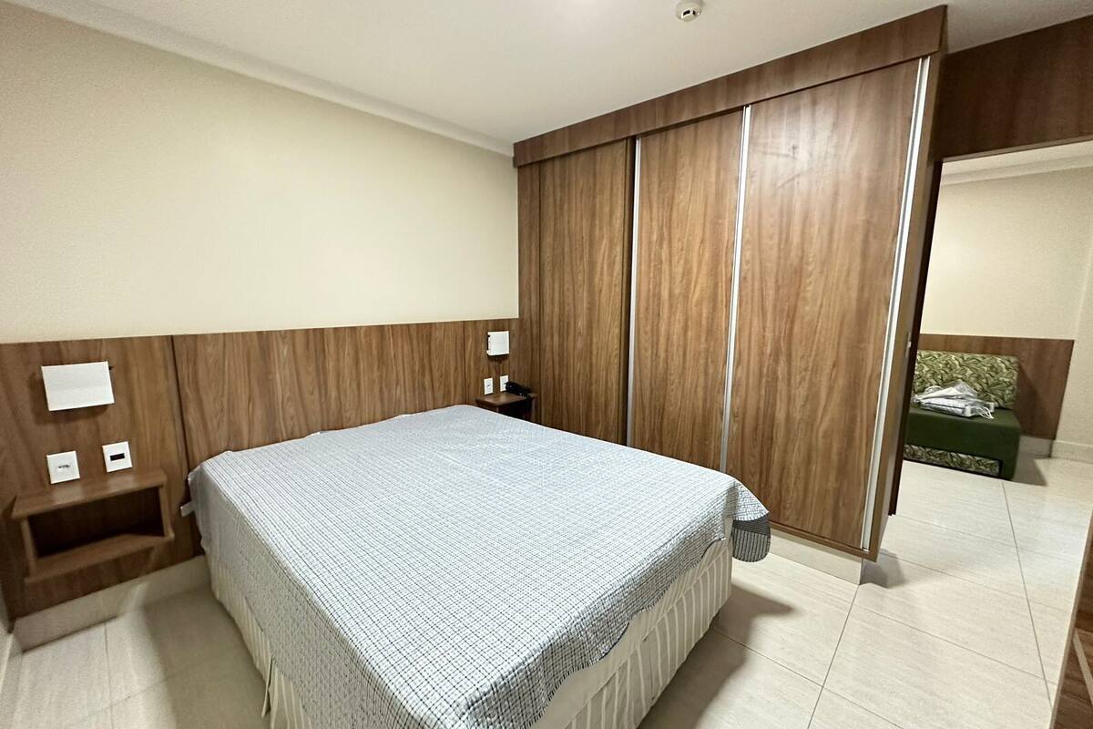 A bedroom with a bed, wooden wardrobe, bedside tables, and a green sofa in the corner.