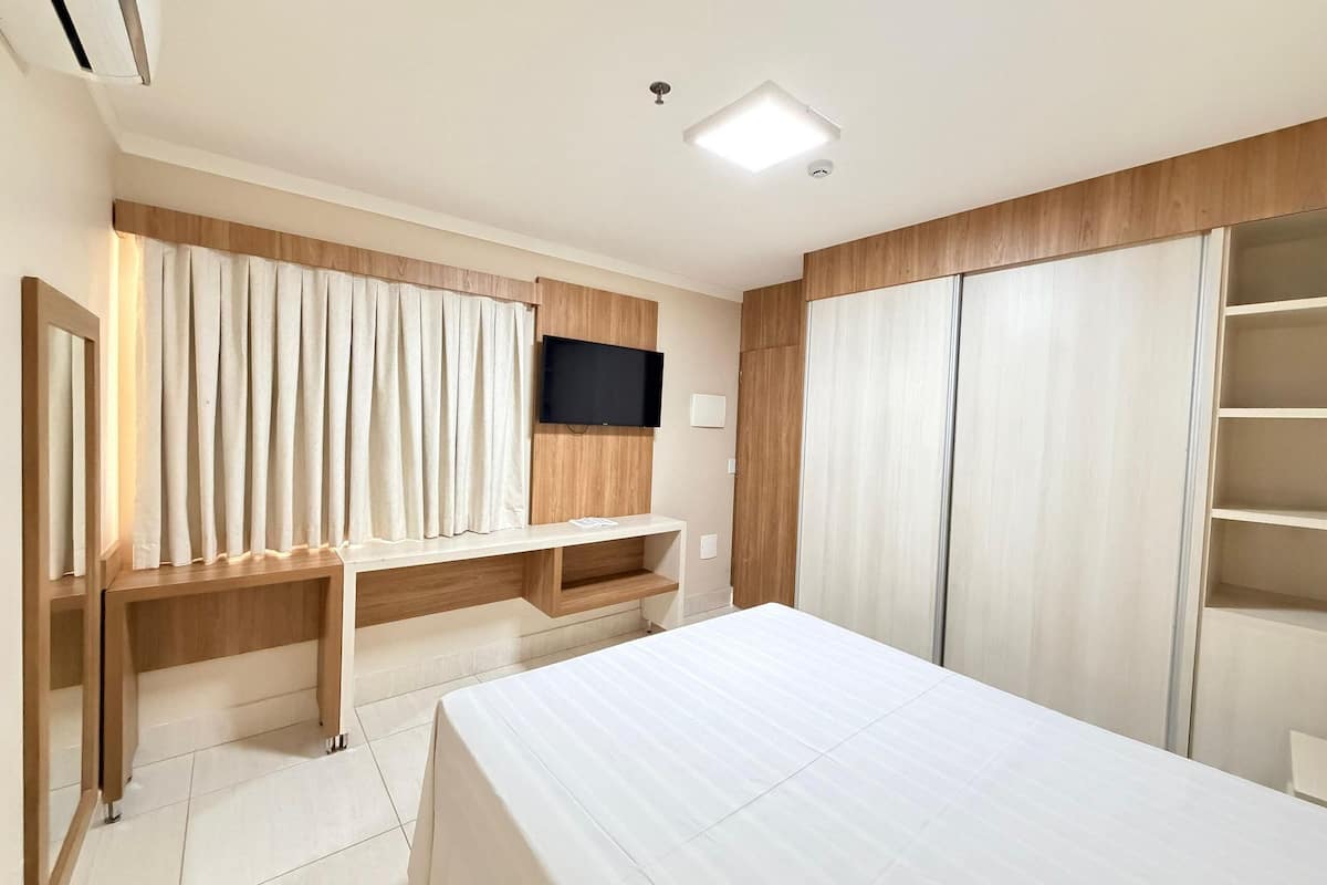 A hotel room with a bed, a desk, a TV, a wardrobe, and a window with curtains.