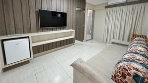 Habitació d'hotel moderna amb televisió de pantalla plana, mini-nevera, sofà i estriatge al llit.
