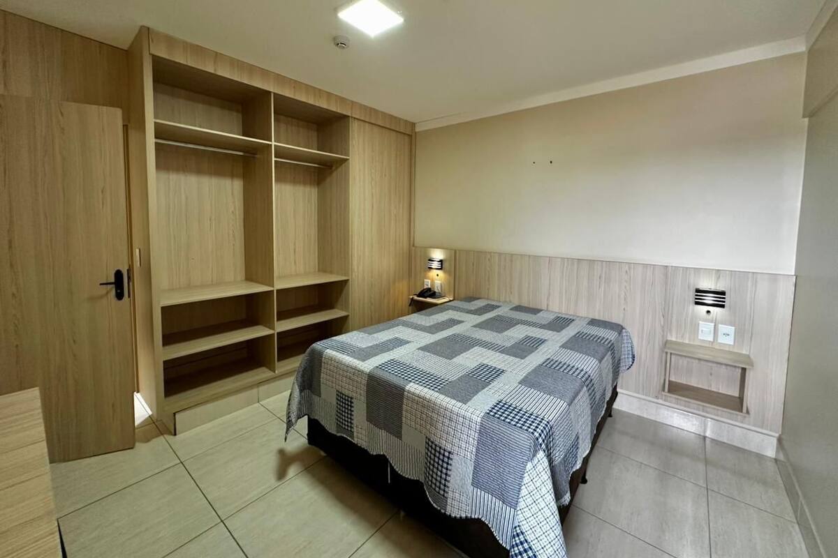 A bedroom with a bed, wooden wardrobe, and a bedside table with a lamp.