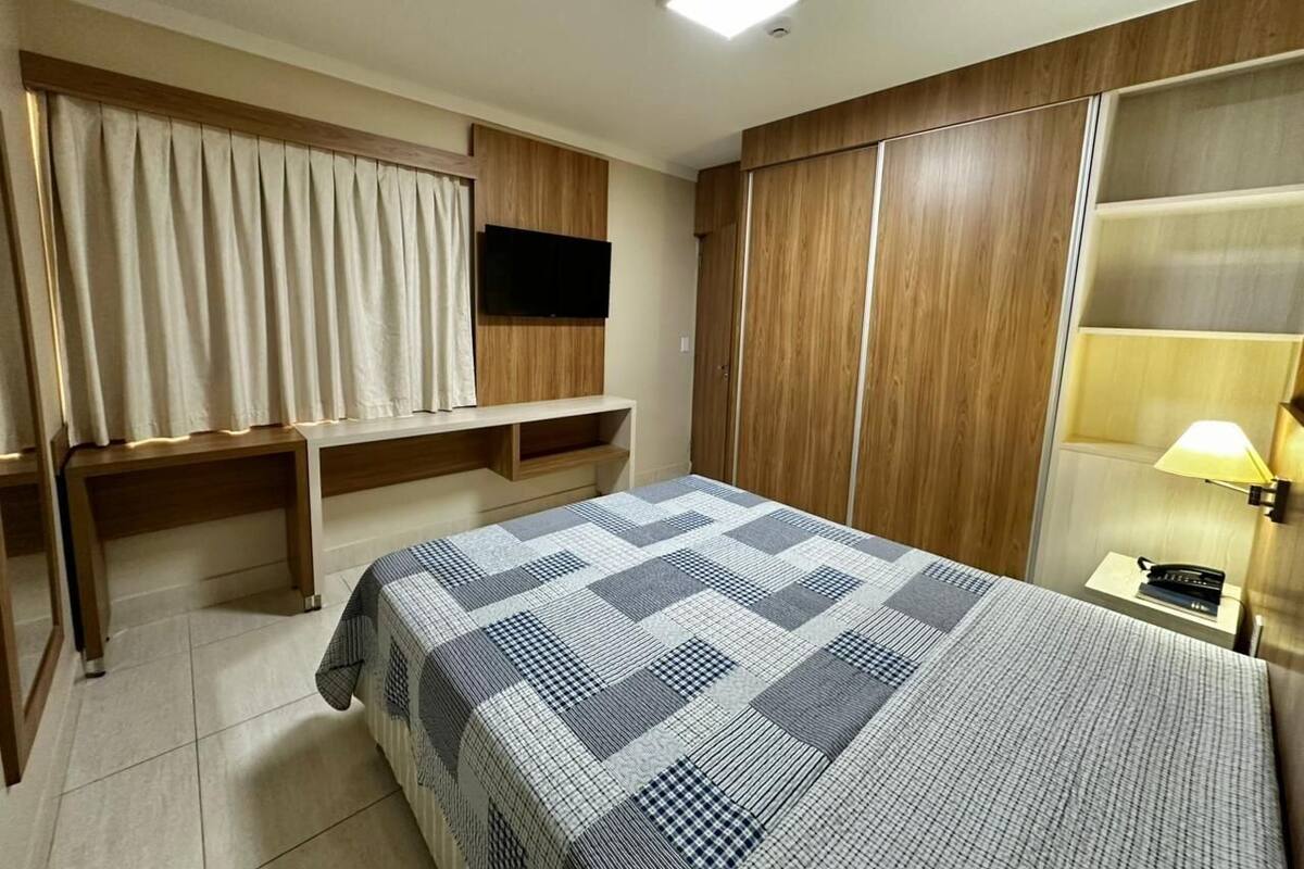 A hotel room with a bed, a TV mounted on the wall, a desk, and a wardrobe.