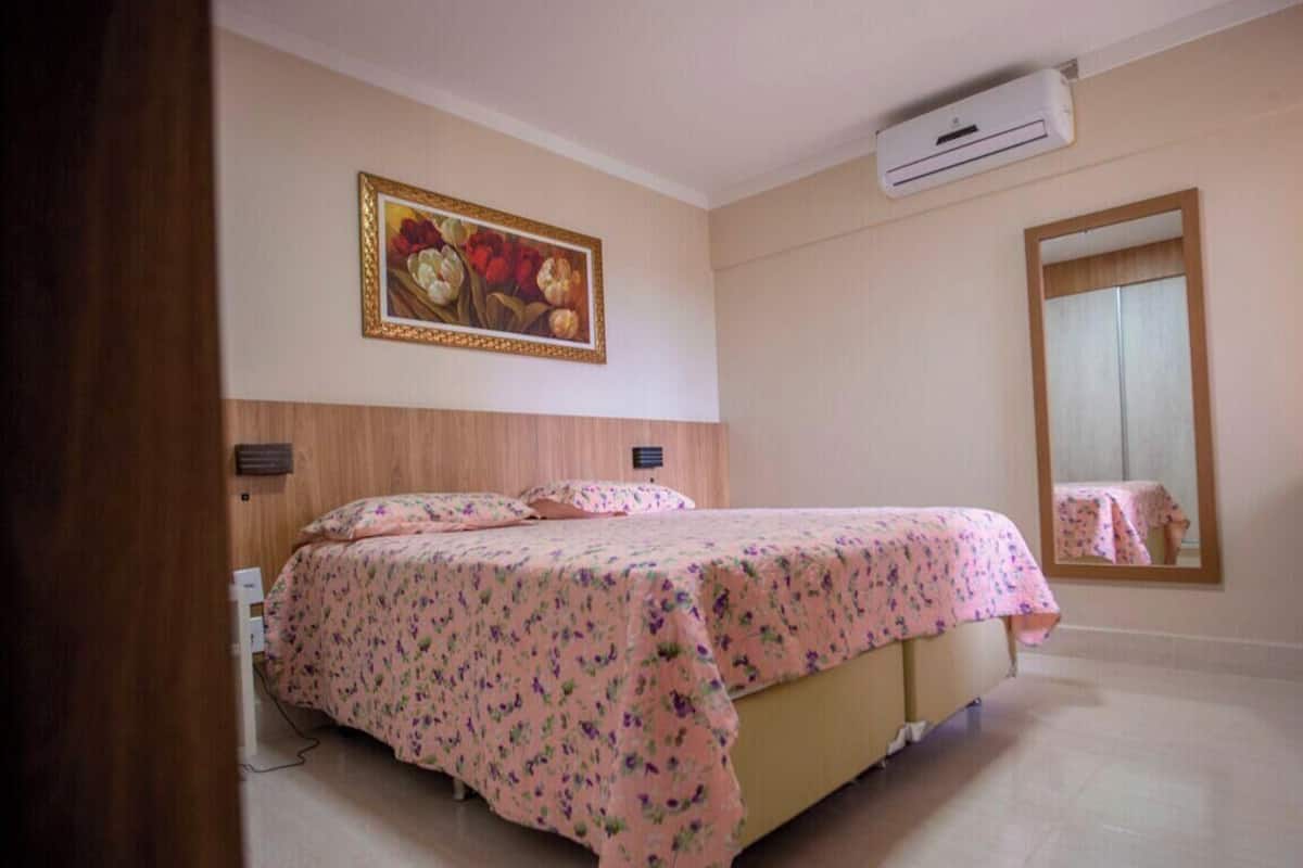A bedroom with a bed, an air conditioning unit, a painting, and a door.