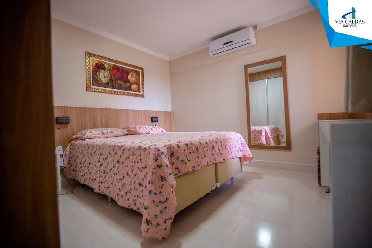 A bedroom with a bed, an air conditioning unit, a mirror, and a painting on the wall.