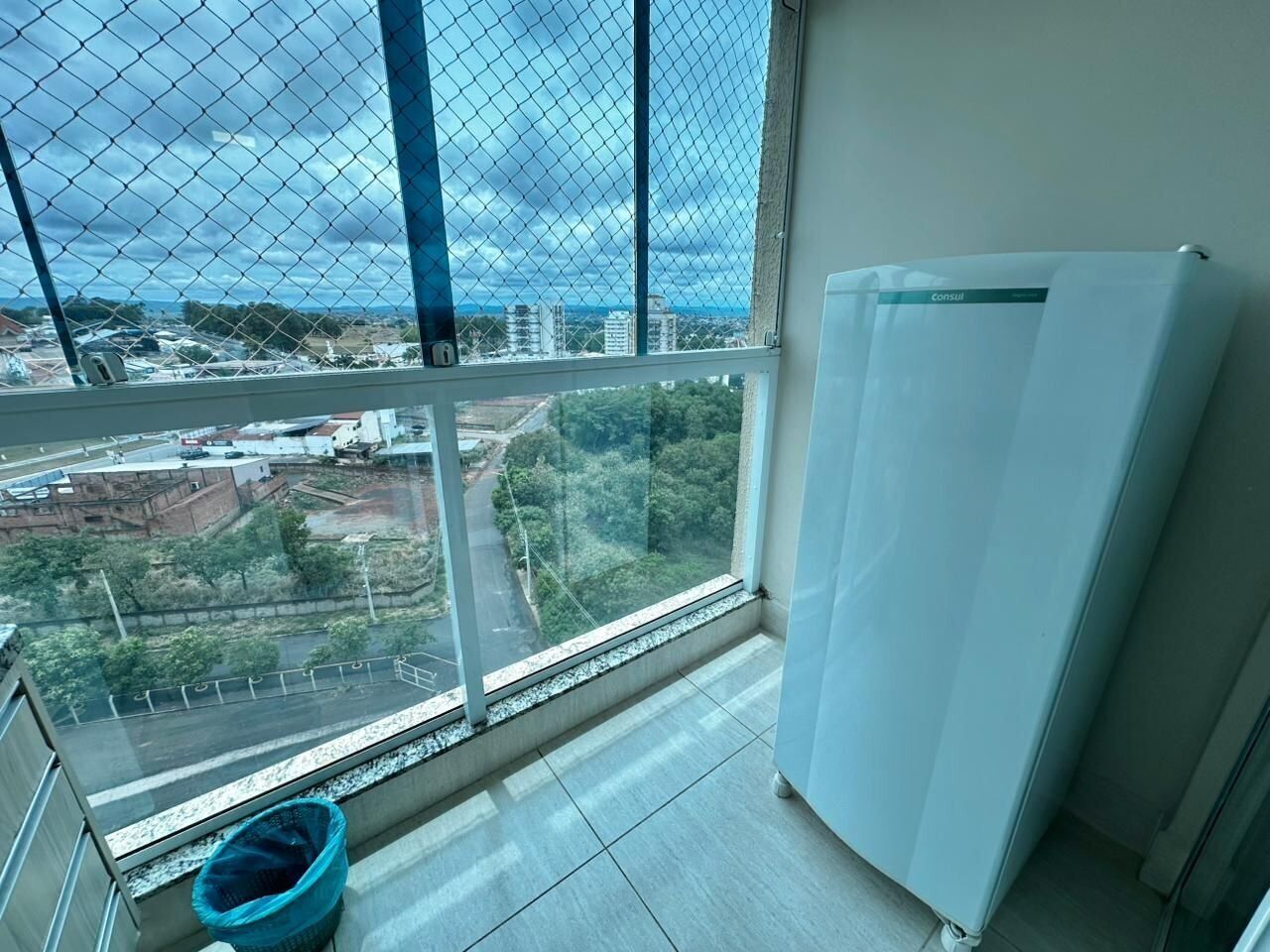 Una habitación con un ventanal grande, un refrigerador blanco y un basurero azul.
