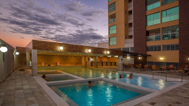 Zona d'una piscina amb diverses piscines, un espai de seients cobert i un edifici amb façana de maó.