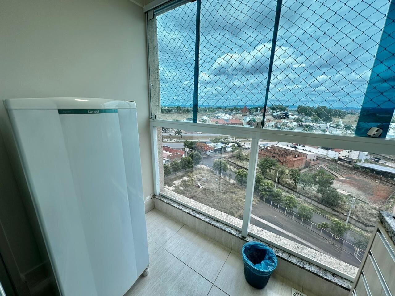 Uma varanda com vista para a paisagem urbana, uma geladeira branca e um balde azul.