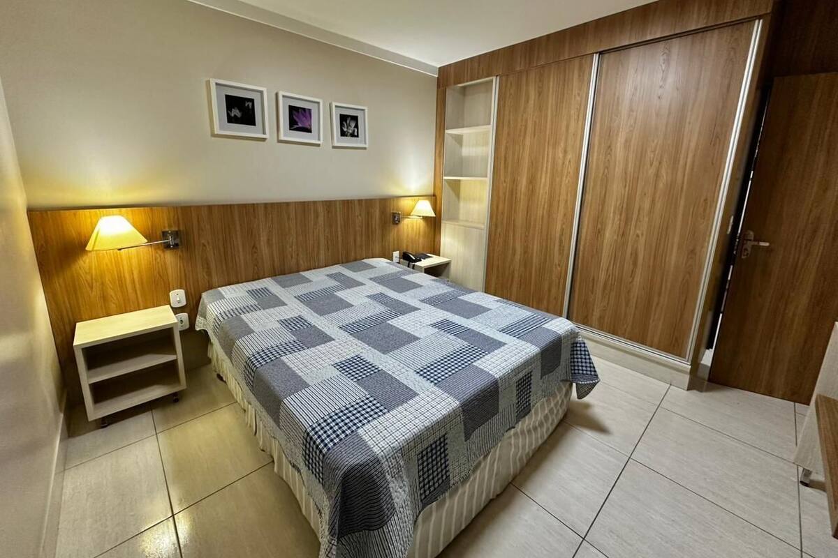 A bedroom with a bed, bedside lamps, a wooden wardrobe, and a small shelf.