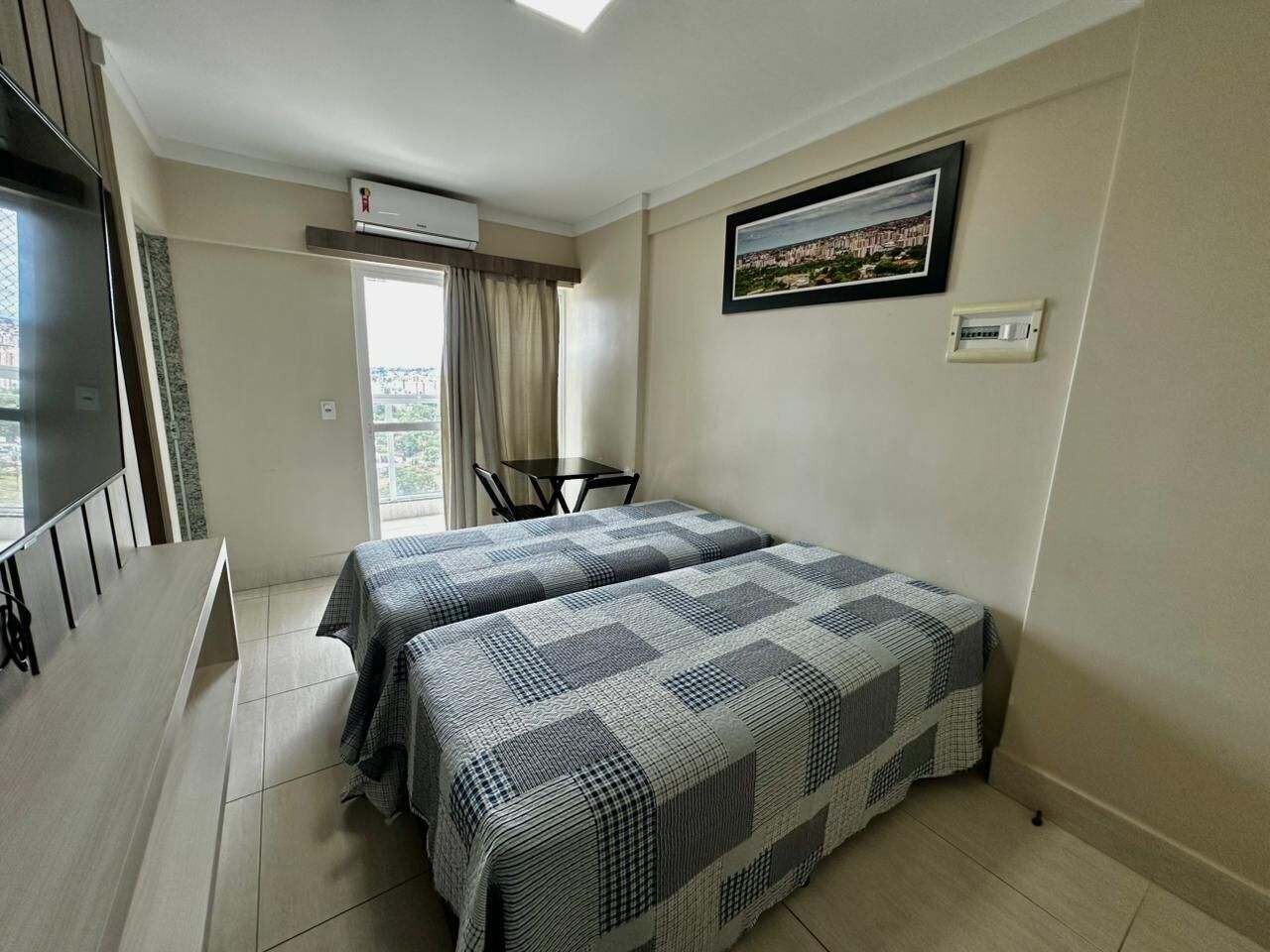 Une chambre d’hôtel avec deux lits, une télévision, une petite table et une fenêtre avec des rideaux.