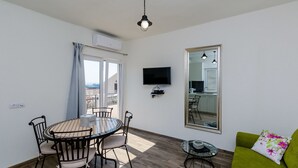 A room with a dining table, chairs, a green sofa, a TV, and a large mirror. - Apartments Life (Dubrovnik)