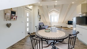 A modern kitchen with a dining area, featuring a round table with chairs, a built-in oven, and a TV. - Apartments Life (Dubrovnik)