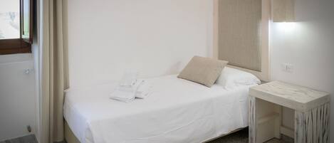 A neatly made bed with white linens, a small bedside table, and a window with curtains.