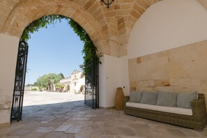 Une cour ouverte avec un sol en pierre, un canapé en osier agrémenté de coussins et un grand vase.