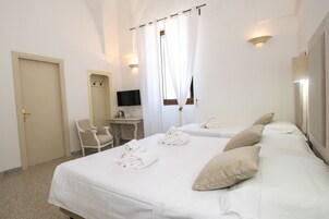 Habitación de hotel con dos camas, un escritorio, una silla, un televisor y un ventanal con cortinas.