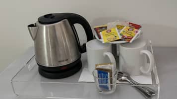 A stainless steel kettle, two white mugs, a glass cup with a tea bag, and a tray with packets of tea and sugar.