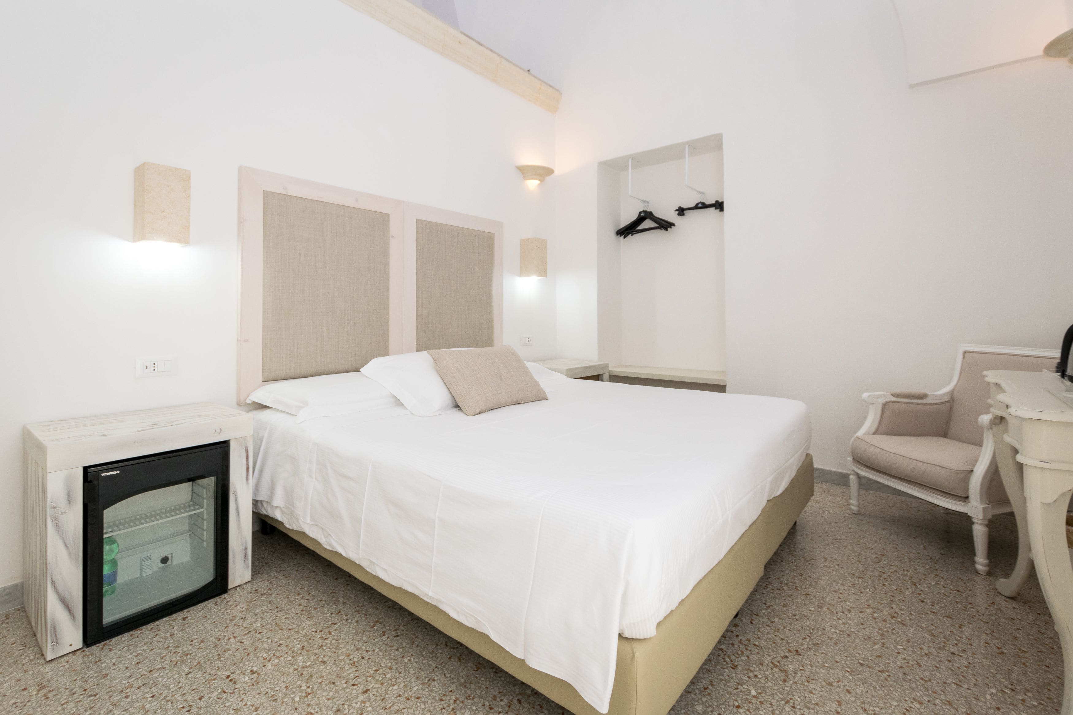 Une chambre d’hôtel équipée d’un lit, d’un petit réfrigérateur, d’une chaise et d’un porte-manteau fixé au mur.