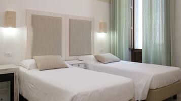A hotel room with two single beds, a bedside table, a nightstand, and a window with curtains.