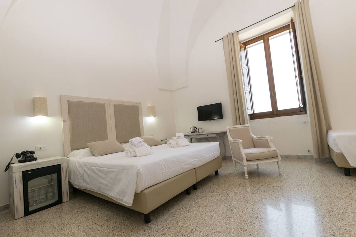 A hotel room with a bed, a desk, a chair, a TV, and a window with curtains.