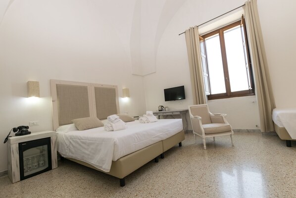 Une chambre d’hôtel avec un lit, un bureau, une chaise, une télévision et une fenêtre avec des rideaux.