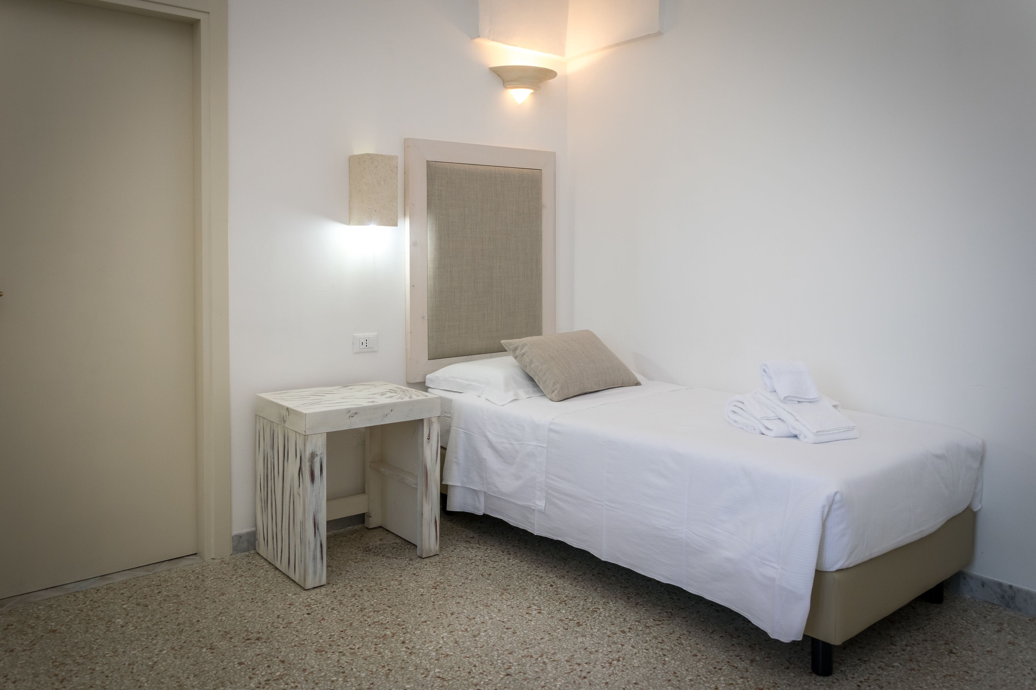 Un dormitorio minimalista con una cama individual, una mesita de noche pequeña y un aplique de pared.