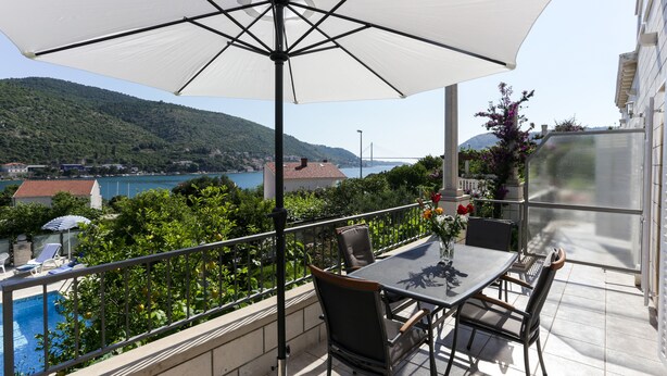 A balcony with a table and chairs, overlooking a pool and a scenic view of a lake and mountains. - Villa Celenca (Dubrovnik)