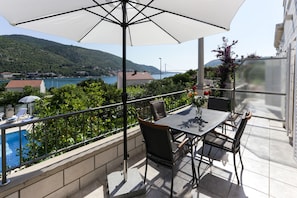 Varanda com mesa e cadeiras, vista para uma piscina e paisagem cénica de um lago e montanhas.