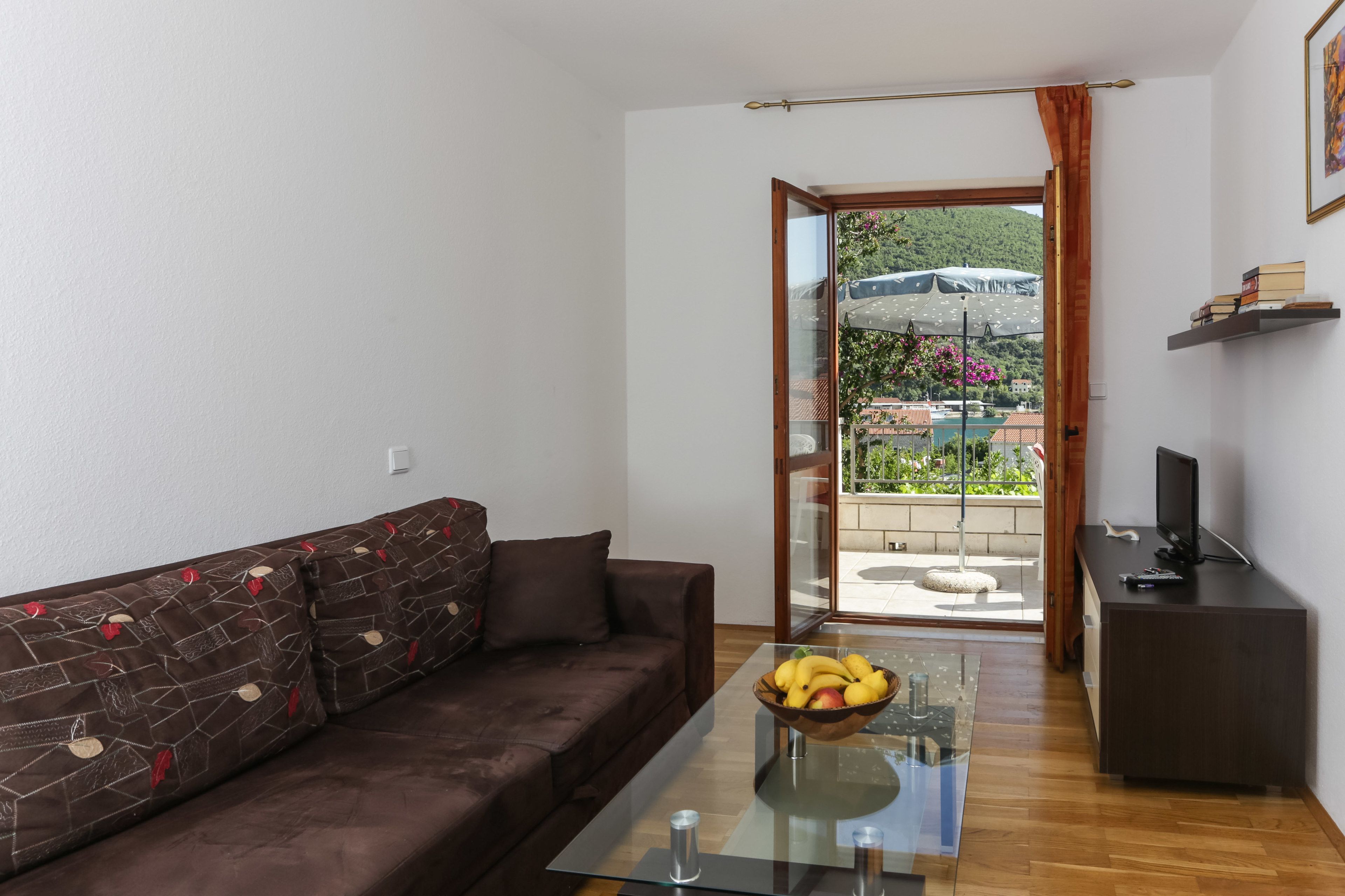 A modern living room with a brown sofa, a glass coffee table with fruit, and a TV on a dark wooden cabinet.