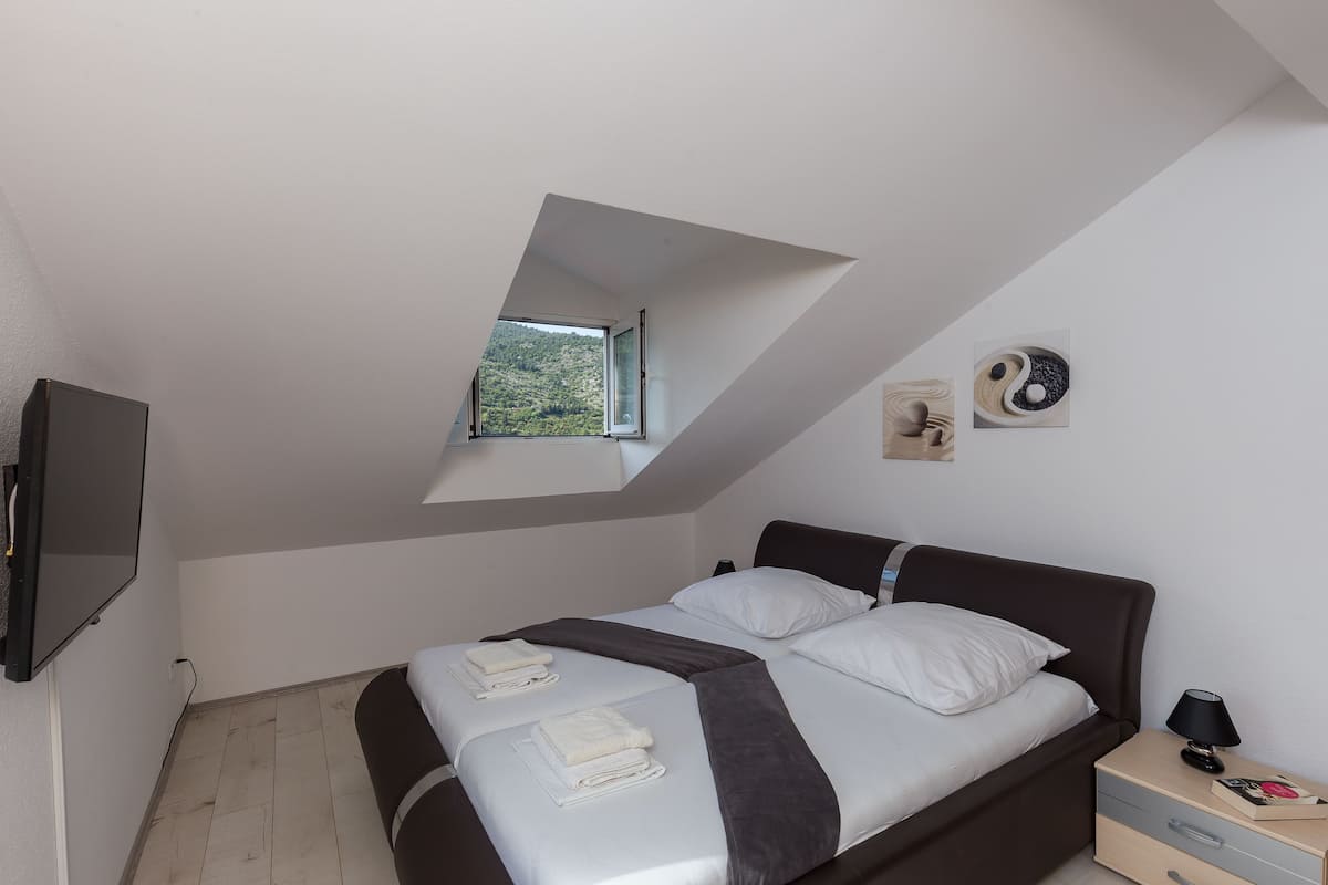 A modern bedroom with a bed, a nightstand, a TV, a small window, and a Zen-inspired wall art piece.